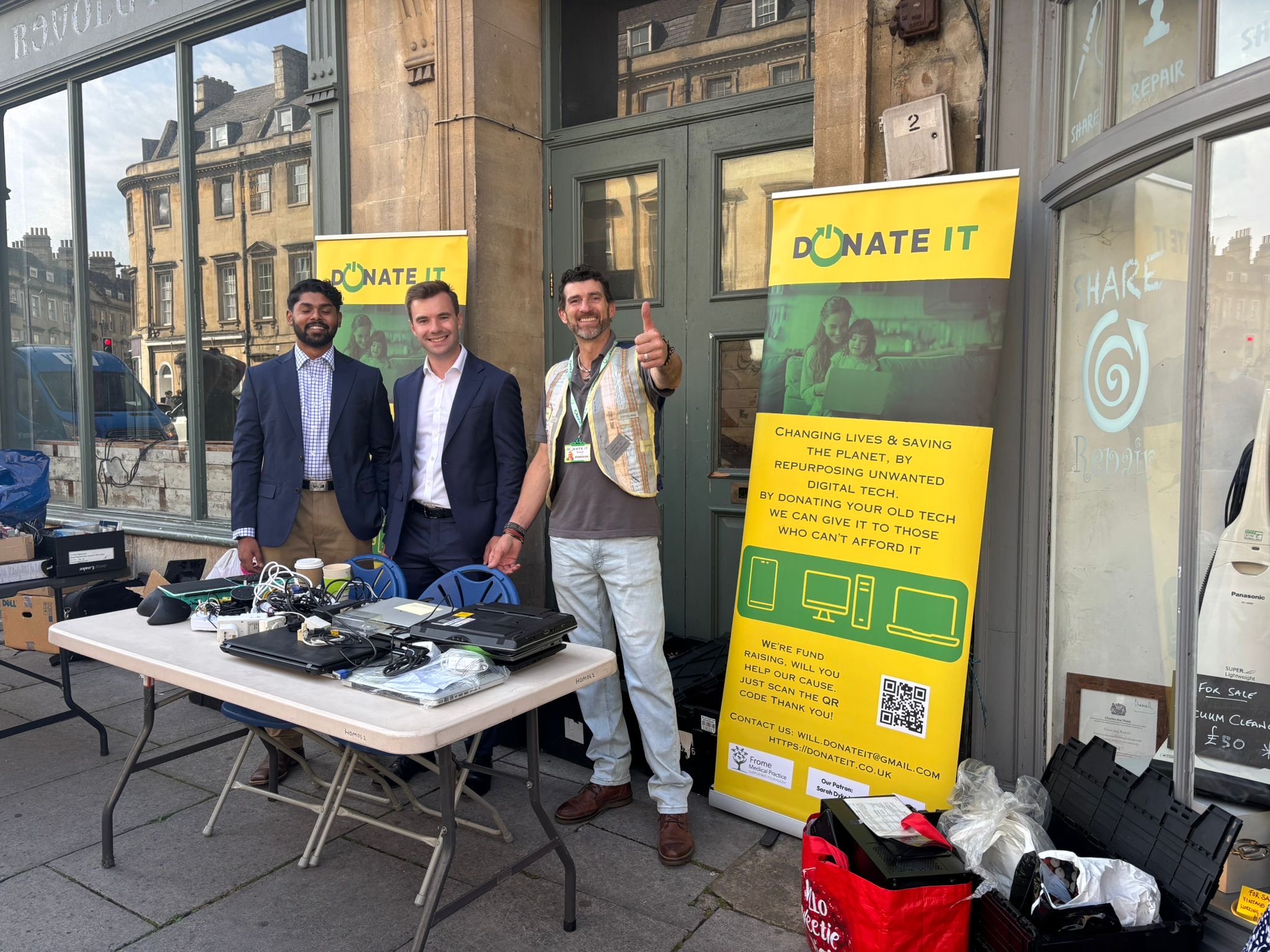 Tech Amnesty July | three men standing at a stall collecting tech donations, and smiling | phones now offered thanks to Donate IT