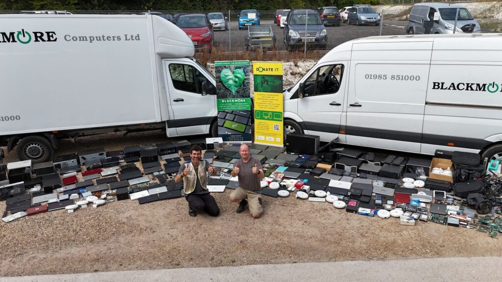 two men kneeling in front of 200 items of tech laid out in front of two white vans, giving thumbs up | Tech Amnesty July