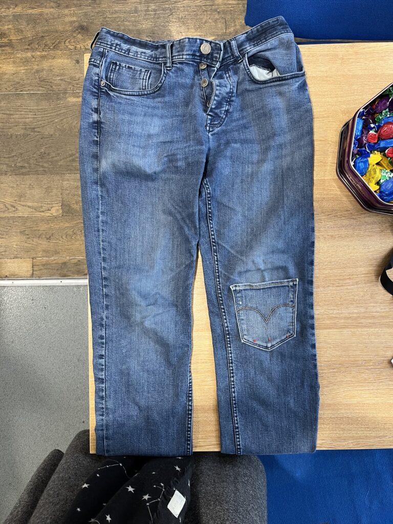 a pair of jeans with a visible mend on the knees, a pocket from another pair of jeans covers a patch on the knee.